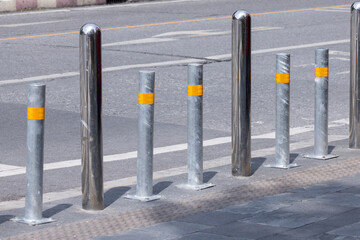 A row of metal poles with yellow stripes. stainless steel bollards on footpath.