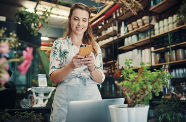 Laptop, phone and text message with florist woman at desk in small business for communication or ecommerce. Computer, sales and smile with happy employee in plant nursery for green retail startup