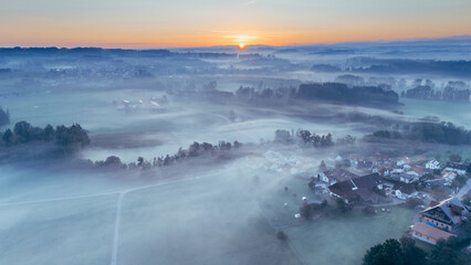 Fototapeta premium Foggy rural landscape with sunrise over small town in Bavaria