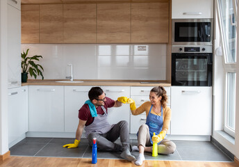 Satisfied couple sitting on floor after kitchen cleaning together