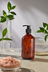 Cosmetic advertising pic in spa space background, an amber pump bottle without label displayed in center, next to a glass bowl of pink salt and glass jar. Green plants decorated in flanked