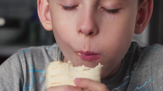 Caucasian boy 10 years old eats delicious burrito, portrait boy eats delicious shawarma