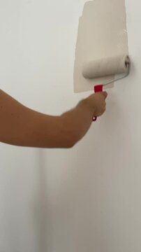Painting wall with beig paint using roller. Construction worker, tool, apartment renovation.