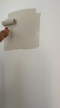 Painting wall with beig paint using roller. Construction worker, tool, apartment renovation.