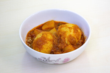 Spicy egg curry or Dim Vuna, cooked with potato, in a white ceramic bowl, placed on a light wooden surface. Boiled dim bhuna is a delicious and traditional dish in Bangladesh.