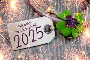 Wooden hang tag and slate with four leaf clover and sparklers with the german words for happy new year - frohes neues jahr 2025 on wooden weathered background	