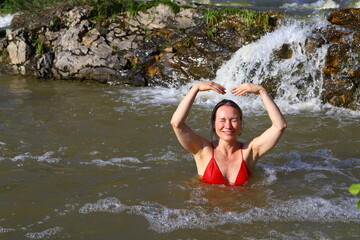 Fototapeta premium Beautiful adult slender woman in a red swimsuit is bathing in a small waterfall.