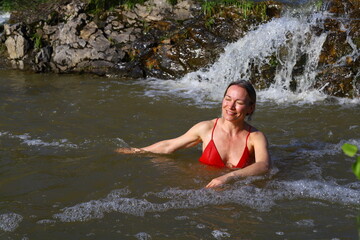 Fototapeta premium Beautiful adult slender woman in a red swimsuit is bathing in a small waterfall.