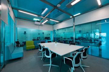 Empty and modern conference room with a large white table and ergonomic chairs, illuminated by a cool blue light
