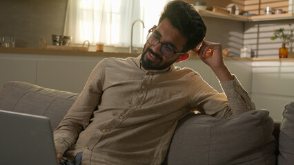Fototapeta premium Shocked upset Indian Arabian man guy business work from home kitchen negative bad result worried anxious male freelancer on couch sofa read laptop notification computer problem fail difficult crisis