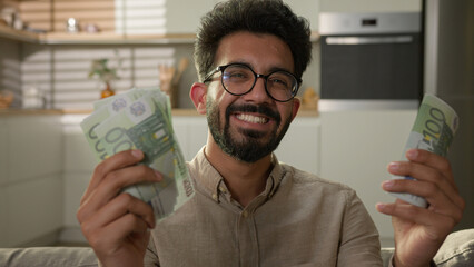 Happy Indian Arabian man rich businessman cash owner celebrate money win count dollars banknotes salary growth wealth finance profit earn budget financial success smiling 30s guy proud at home kitchen