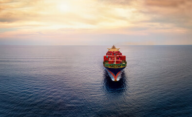 Aerial front view of a big cargo container carrier ship sailing over the ocean during sunset time...