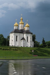 A white stone church stands on a rise near the road. White church with golden domes and crosses. 