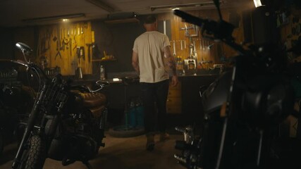 Blond guy in a white T-shirt mechanic works and repairs a motorcycle in his workshop