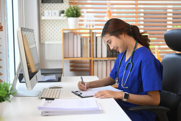 Smiling female doctor in a blue scrubs reviewing document in medical office