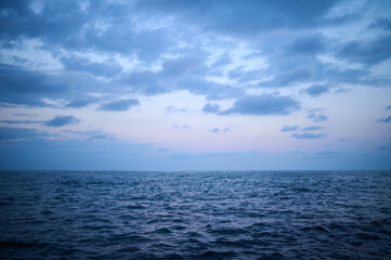Endless blue horizon over the calm ocean at twilight with soft clouds creating a tranquil atmosphere