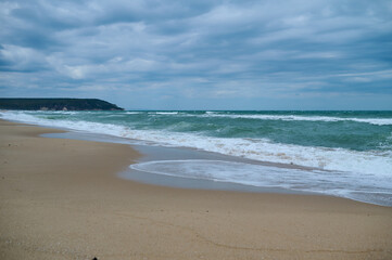 Obraz premium Stunning coastal view showcasing gentle waves lapping at the sandy shore under a cloudy sky at a tranquil beach