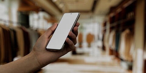 Asian male using smartphone with a blank white screen. Clothing store, retail, interior apps mockup. Vertical phone orientation