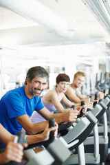 Obraz premium Portrait, spin class or happy man cycling in gym, training and exercise for group, health or fitness. Smile, mature or people riding bicycle machine for cardio, strong legs or power for body workout