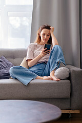 Woman with smartphone mobile app or website information using phone home sofa