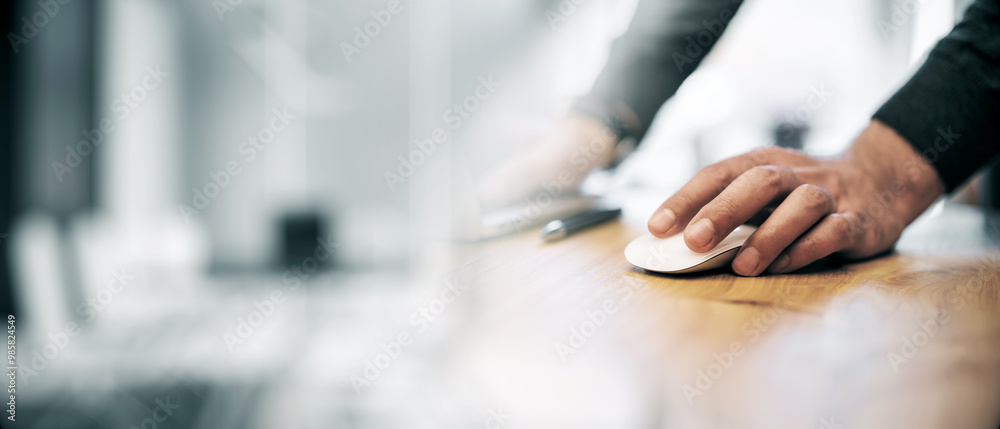 Poster Closeup of a man's hand using a computer mouse on a wooden desk in an office setting.