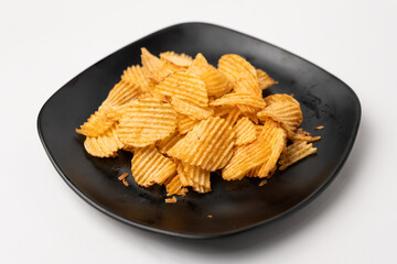 A pile of ridged potato chips on a black plate
