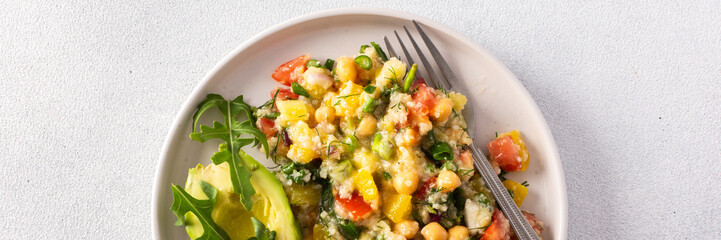 A vibrant vegetarian salad featuring boiled millet, chickpeas, fresh vegetables, and avocado, drizzled with olive oil for a delicious and healthy meal, banner