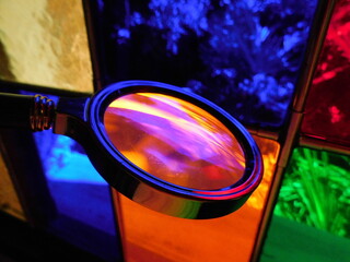 Die Lupe reflektiert bunte Gläser im Hintergrund (blau, orange)