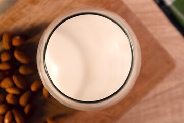 Top view of a glass of almond milk and almonds on wooden table