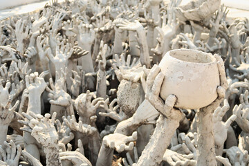 A sculpture of two hands holding a bowl surrounded by hundreds of outreaching hands at the bridge of "the cycle of rebirth", at the White Temple, Wat Rong Khun, Chiang Rai, Thailand