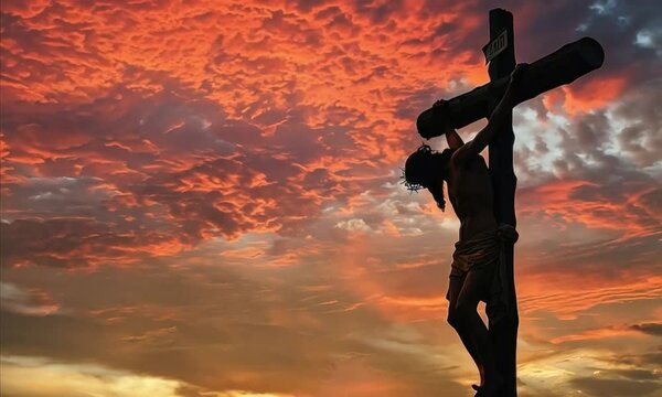 Silhouette of a man crucified on a cross against a fiery sunset sky