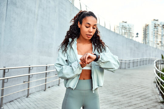 Beautiful young athlete woman looking at smartwatch and counting calories burned outdoors in the morning after running.Healthy life,  sport concept.