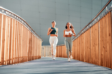 Focused fitness: Two women running outdoors on a modern bridge. Copy space.