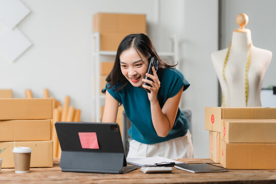 E-commerce Efficiency: Young Asian entrepreneur managing her online business, coordinating orders and logistics over the phone with a cheerful demeanor.