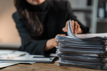 Buried in Paperwork: A businesswoman's hands sift through a towering stack of documents, her face...