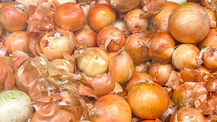 A pile of onions with some of them peeled. The onions are all different sizes and are scattered around the pile