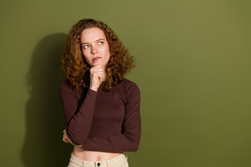 Photo of doubtful unsure girl wear brown shirt arm chin looking empty space isolated green color...