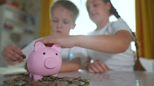 Happy children saving money in piggybank at home. Happy children smiling while learning to save coins. Concept of early financial education. Children using piggybank at home, happy to save together.