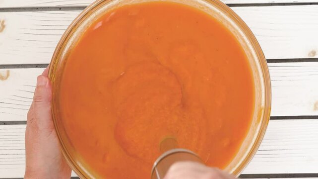 Roasted butternut squash soup recipe, preparation process. Blending roasted vegetables into a puree, adding vegetable stock in a bowl, close-up view