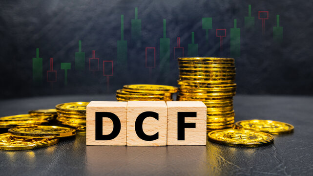 The inscription DCF text on wooden cubes with stack of coin on black background with stock market graph. Business profitability success growth profitability analytics. Business and financial concept.