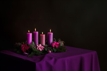 On a table, four burning purple advent candles are set within a circle of fir branches, Christmas religious tradition.