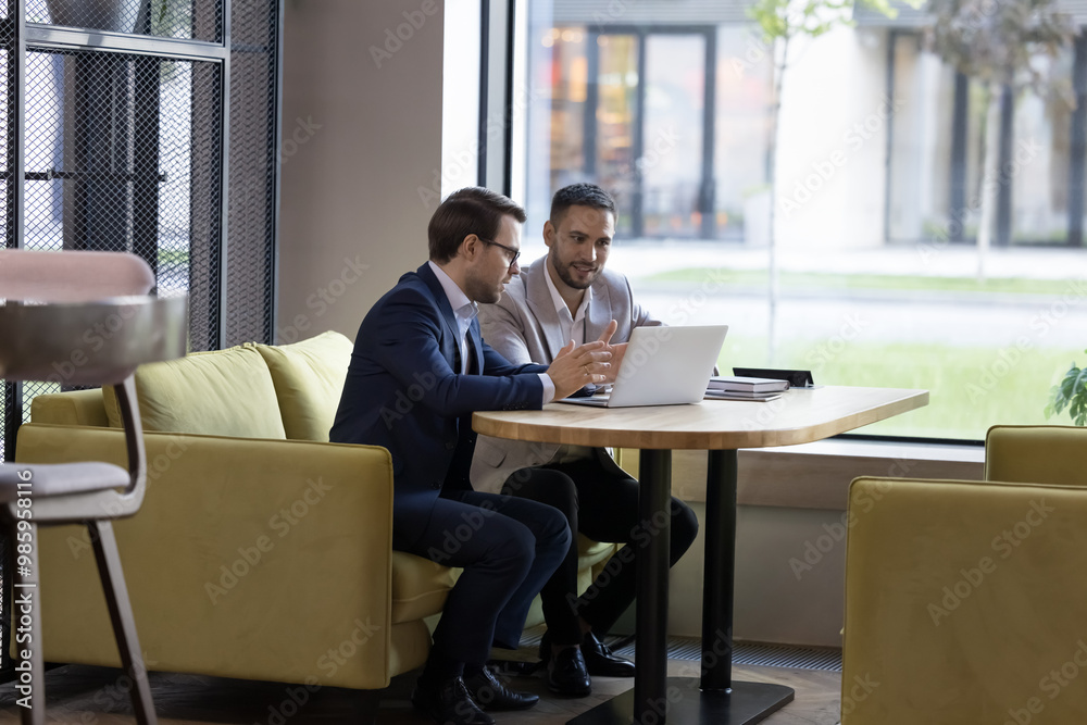 Wall mural two engaged business partners talking at laptop in office cafe, watching online project presentation