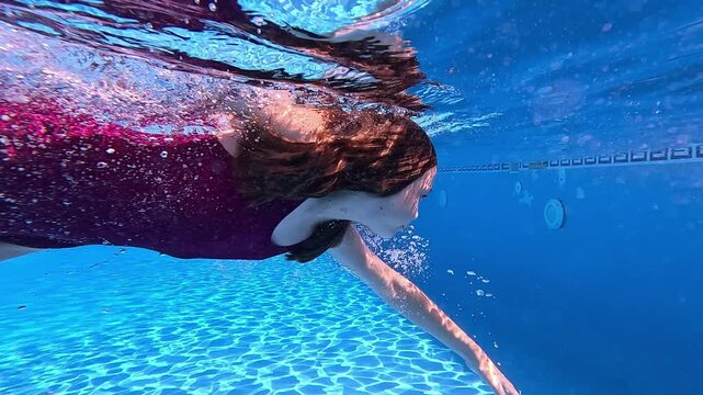 Girl swimming crawl style in a pool with her eyes open. Seen from underwater with a bright clear blue background