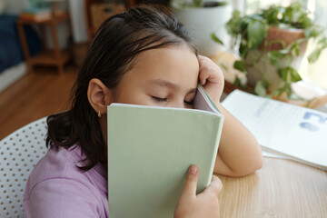 Schoolgirl sitting at desk with notebook and sleeping during her study