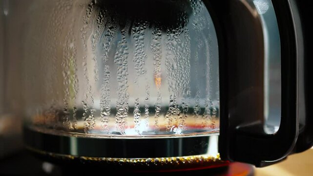 A closeup of a coffee makers carafe shows steam condensing on its glass and drops falling, highlighting coffees importance in our daily routines and its comforting presence at breakfast