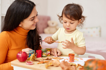 Cute little girl and mom spending good time painting autumn yellow leaves together
