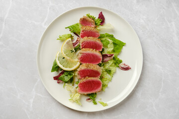 Seared tuna slices served on a bed of fresh greens with lemon garnishes in a modern setting