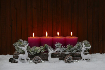 Hintergrund für Weihnachten und Advent. Arrangement zum vierten Advent mit vier roten brennenden Kerzen, Tannenzweigen und Hirschen im Schnee  vor einer winterlichen Kulisse.