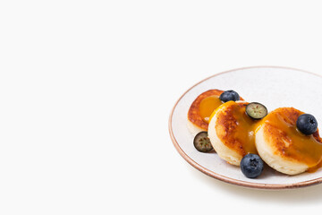 Plate with сottage cheese pancakes or syrniki, fresh blueberries and peach topping on white background. Sweet breakfast or lunch concept