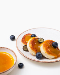 Plate with сottage cheese pancakes or syrniki, fresh blueberries and peach topping on white background. Sweet breakfast or lunch concept